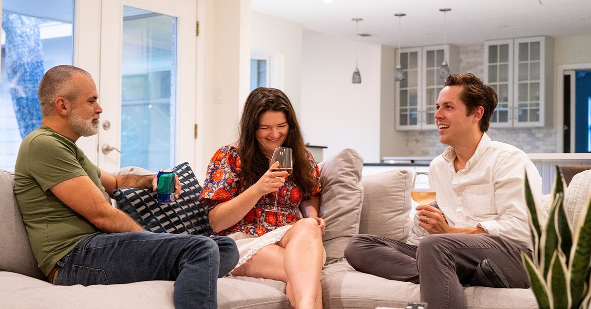 3 people sitting on a couch around a coffee table drinking